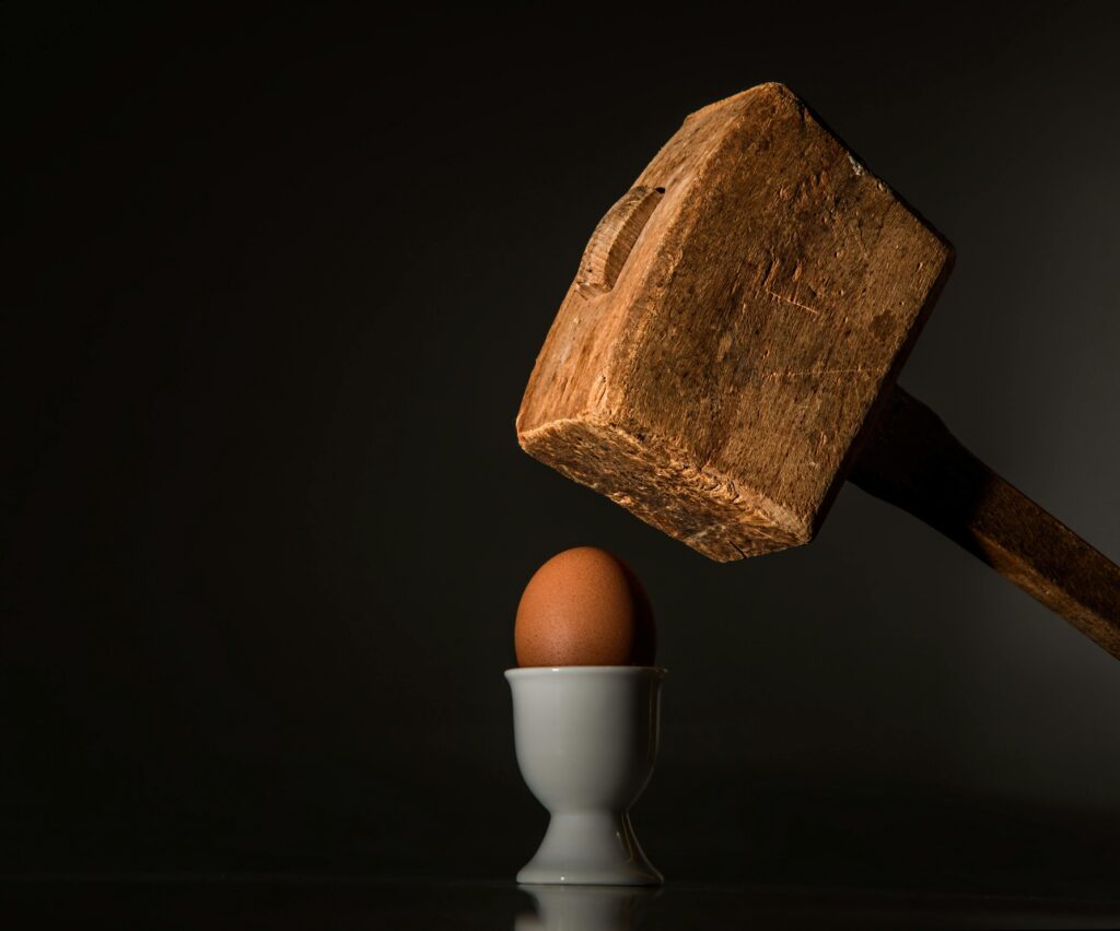 A large wooden hammer being used to crack a soft boiled egg